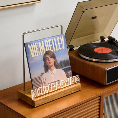 Vinyl record on a 'Now Playing' stand with a turntable in the background