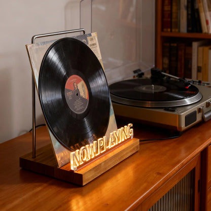 Vinyl record on a 'Now Playing' stand with a turntable in the background