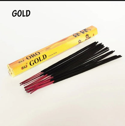 A yellow rectangular box labeled "Oro Gold" next to a spread of black incense sticks with red tips on a white surface.